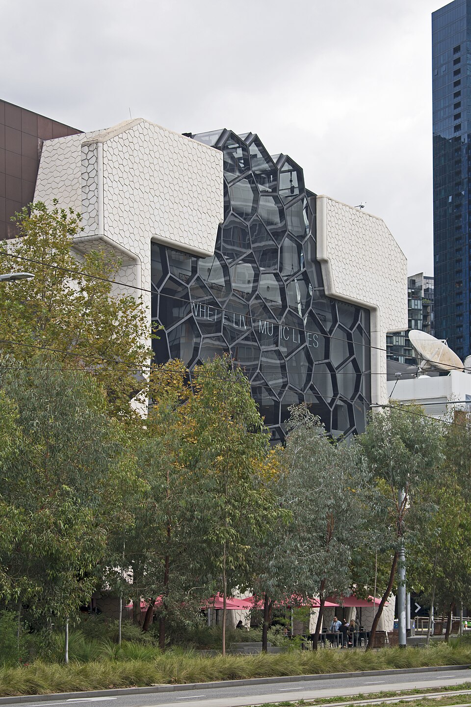Melbourne Recital Centre’s patterned white façade and angular glazing seen above street trees.