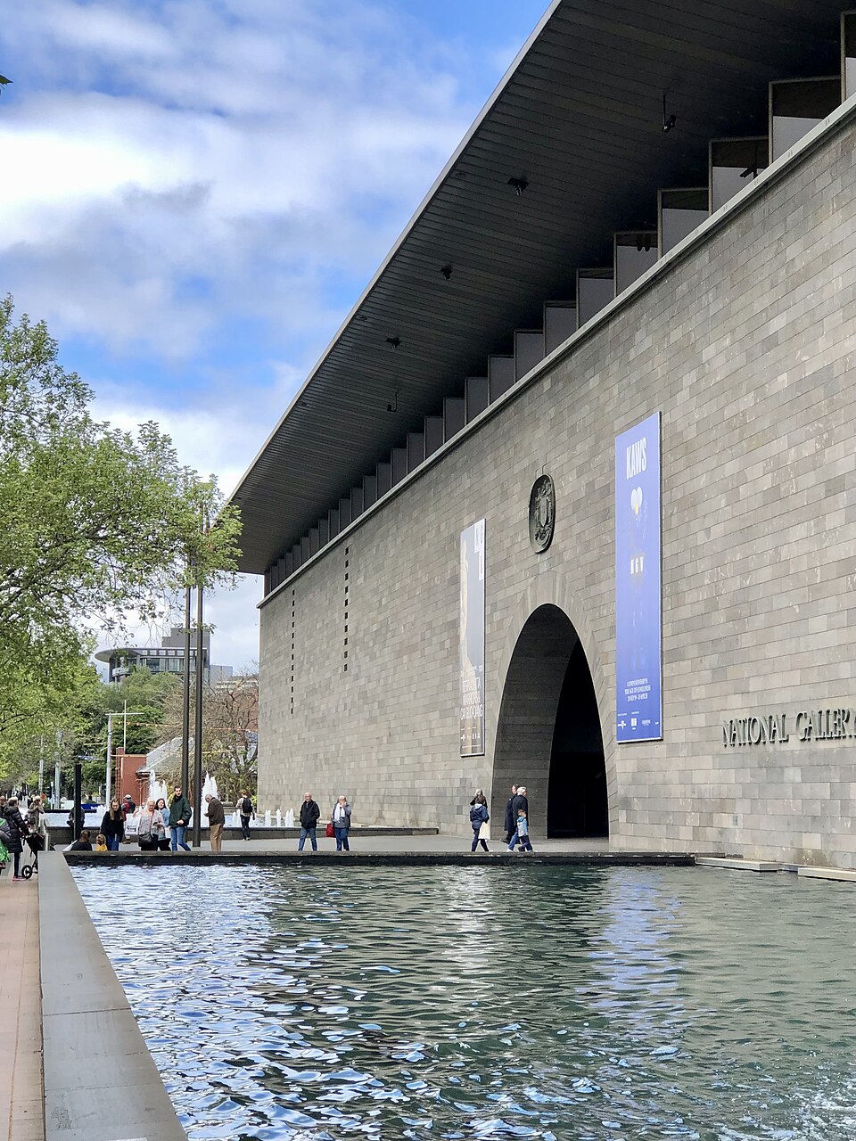 NGV International’s long stone façade and arched entrance beside a reflecting pool.