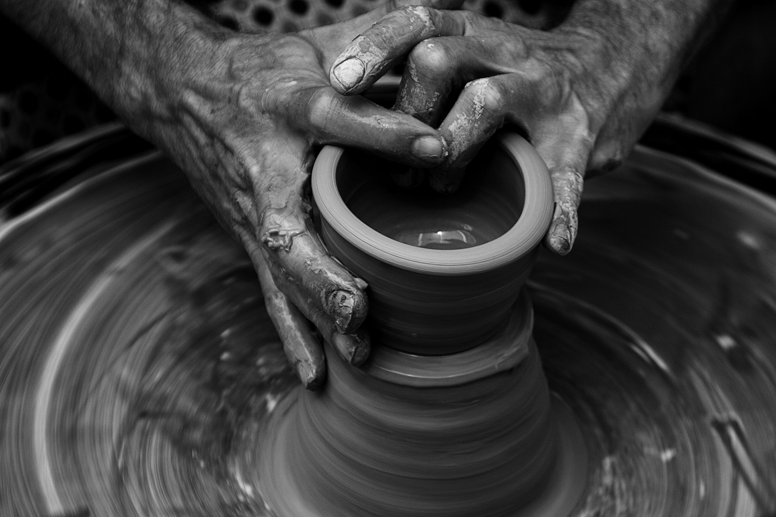 Clay-covered hands shaping the rim of a pot on a spinning pottery wheel.