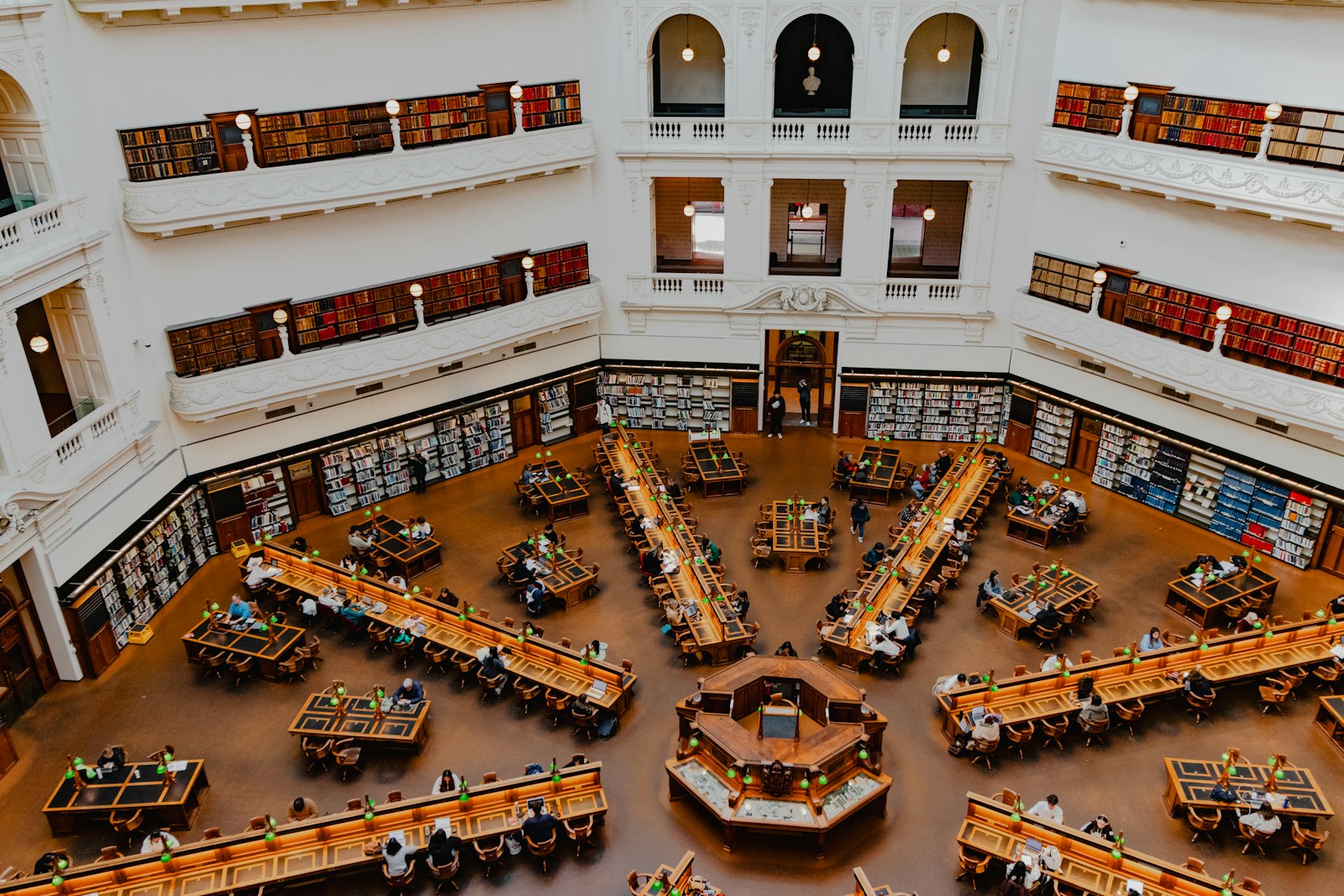 Readers at radial desks beneath the white galleries of State Library Victoria’s La Trobe Reading Room.