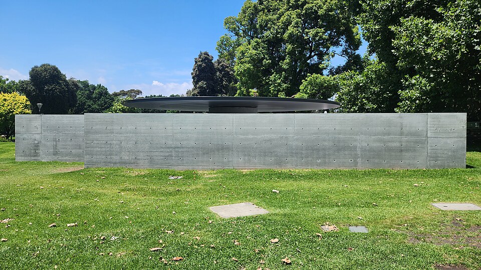 Low concrete walls and a thin circular canopy amid the trees of Queen Victoria Gardens.