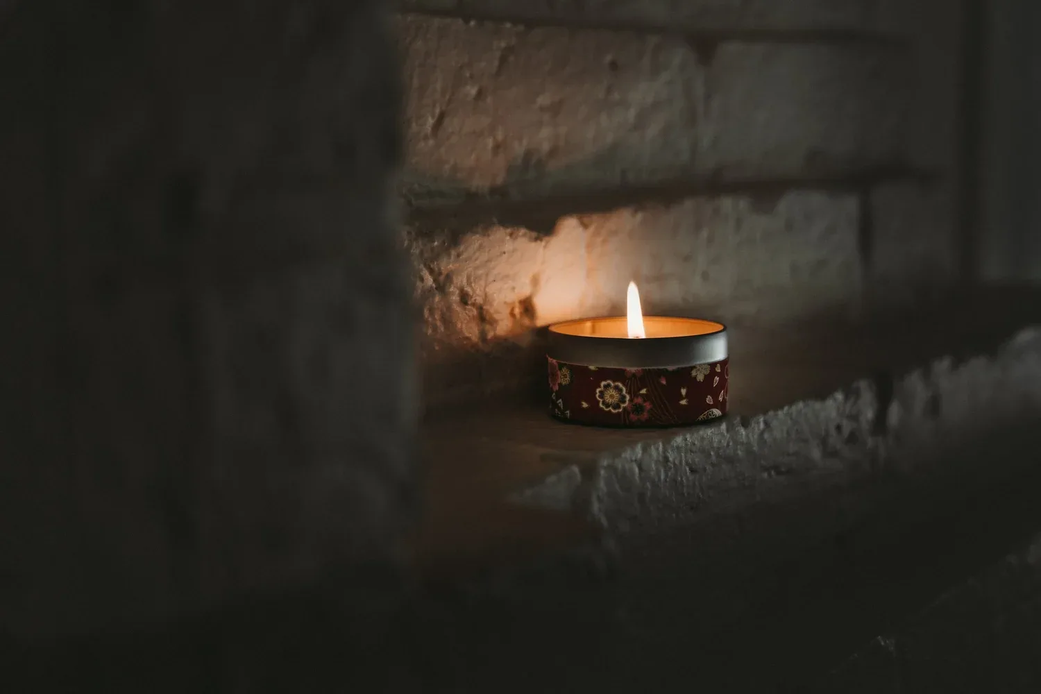 A glowing candle set against a darker wall.