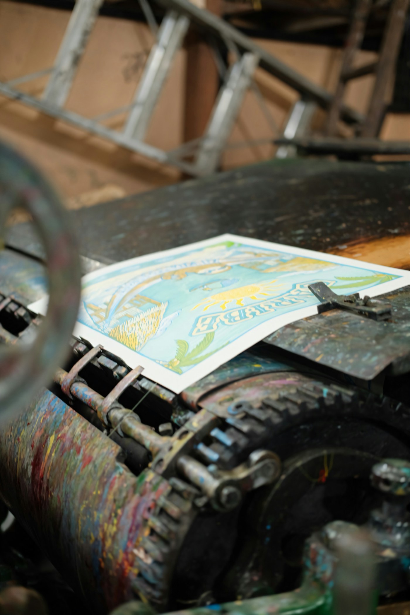 A colourful print on paper rests on the bed of an ink-marked printing press.